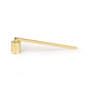 Éteignoir en laiton doré Paddywax posé sur une table avec une bougie, accessoire élégant pour éteindre la flamme sans fumée.