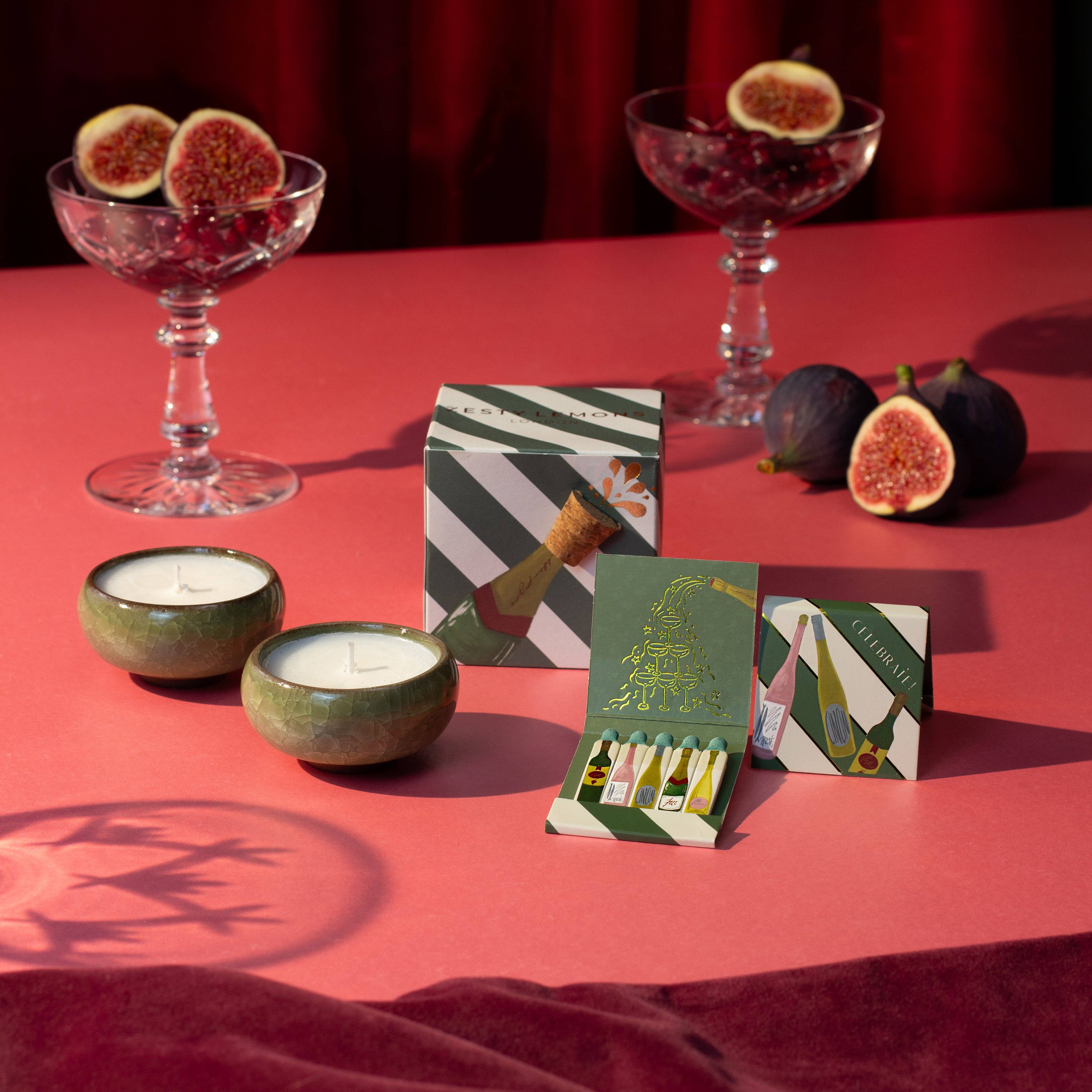 Boîte d’allumettes CELEBRATE de Zesty Lemons, illustrée de bouteilles festives avec allumettes décorées et intérieur doré.