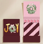 Boîte d’allumettes JOY Zesty Lemons avec couronne de Noël et allumettes rayées bordeaux et rose.